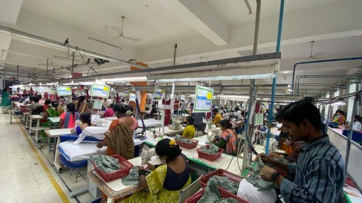 Image showing a garment factory floor with multiple workers operating sewing machines in rows